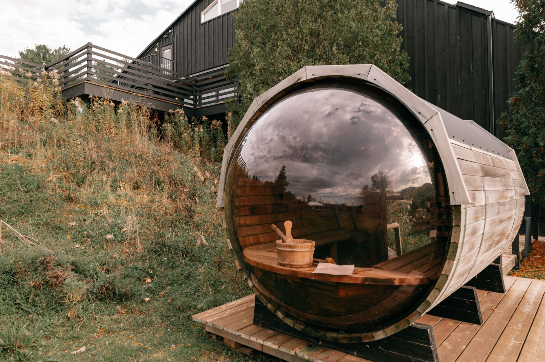 Cedar barrel sauna with rounded walls sitting on a wooden backyard deck at dusk