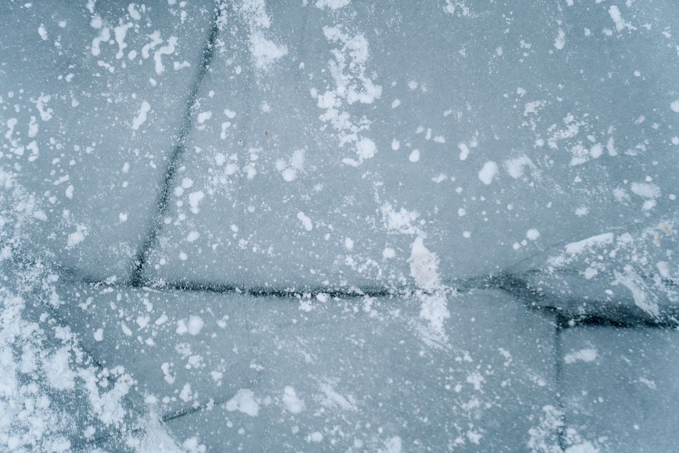 A close-up, top-down view of a cracked icy surface with snow sprinkled on it.