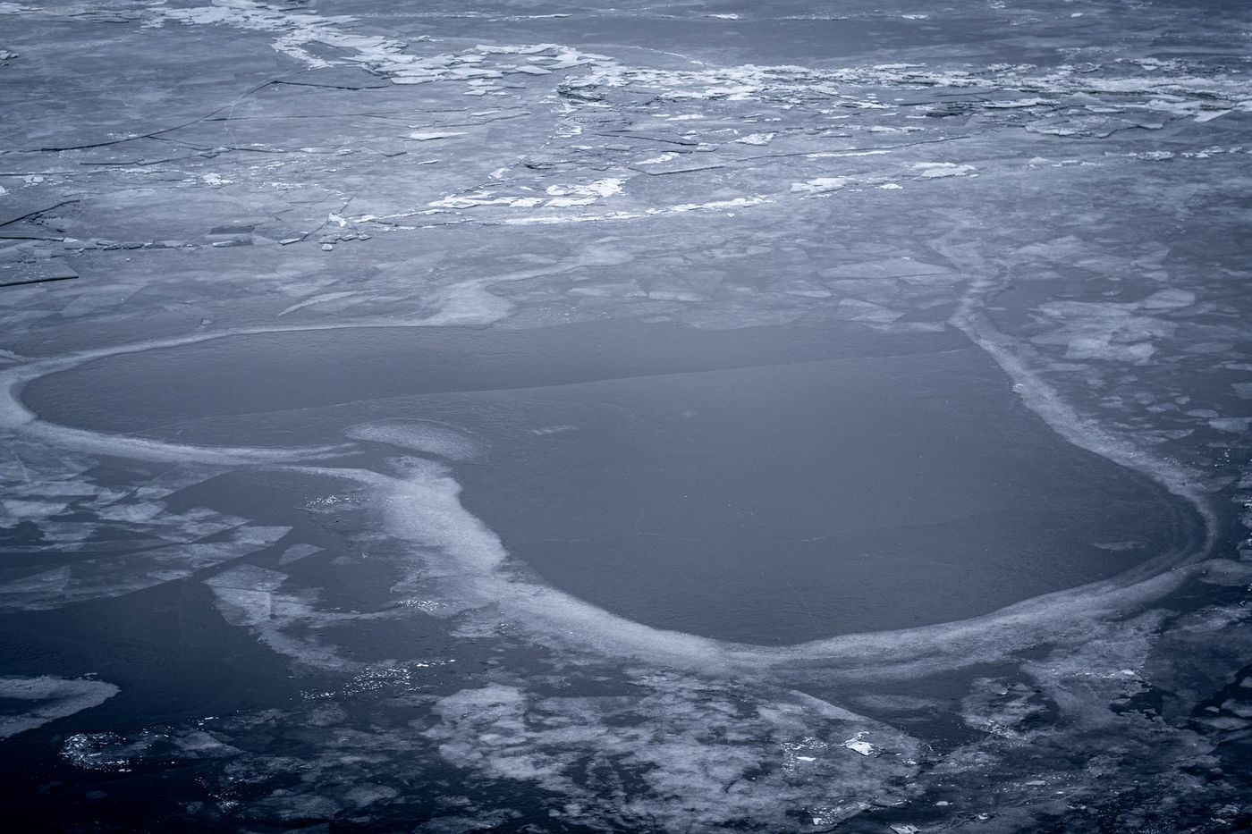 An aerial view of a frozen body of water with a heart-shaped opening in the ice.