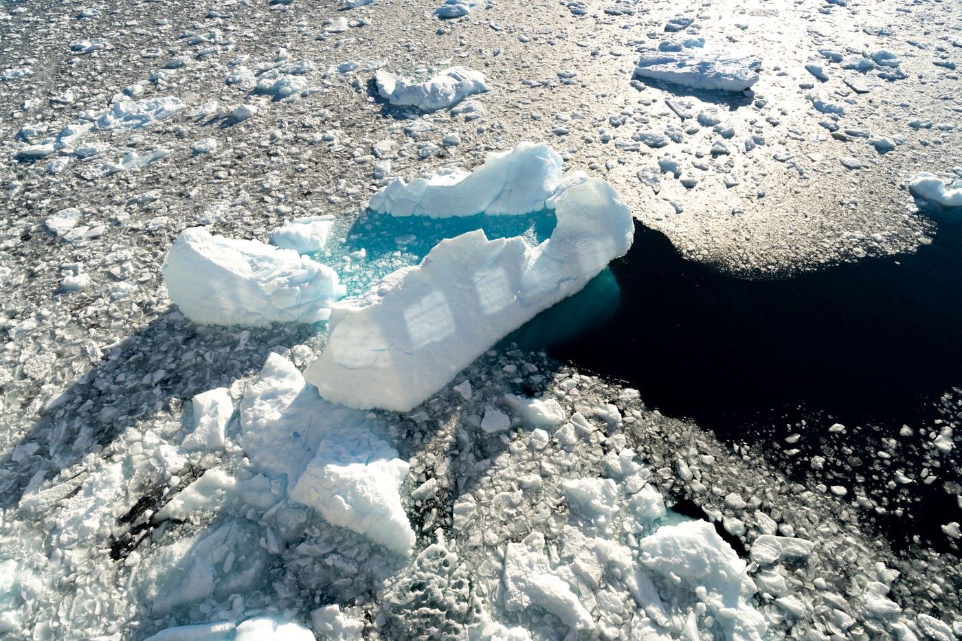 An aerial view of a large iceberg and smaller ice floes floating in the ocean.