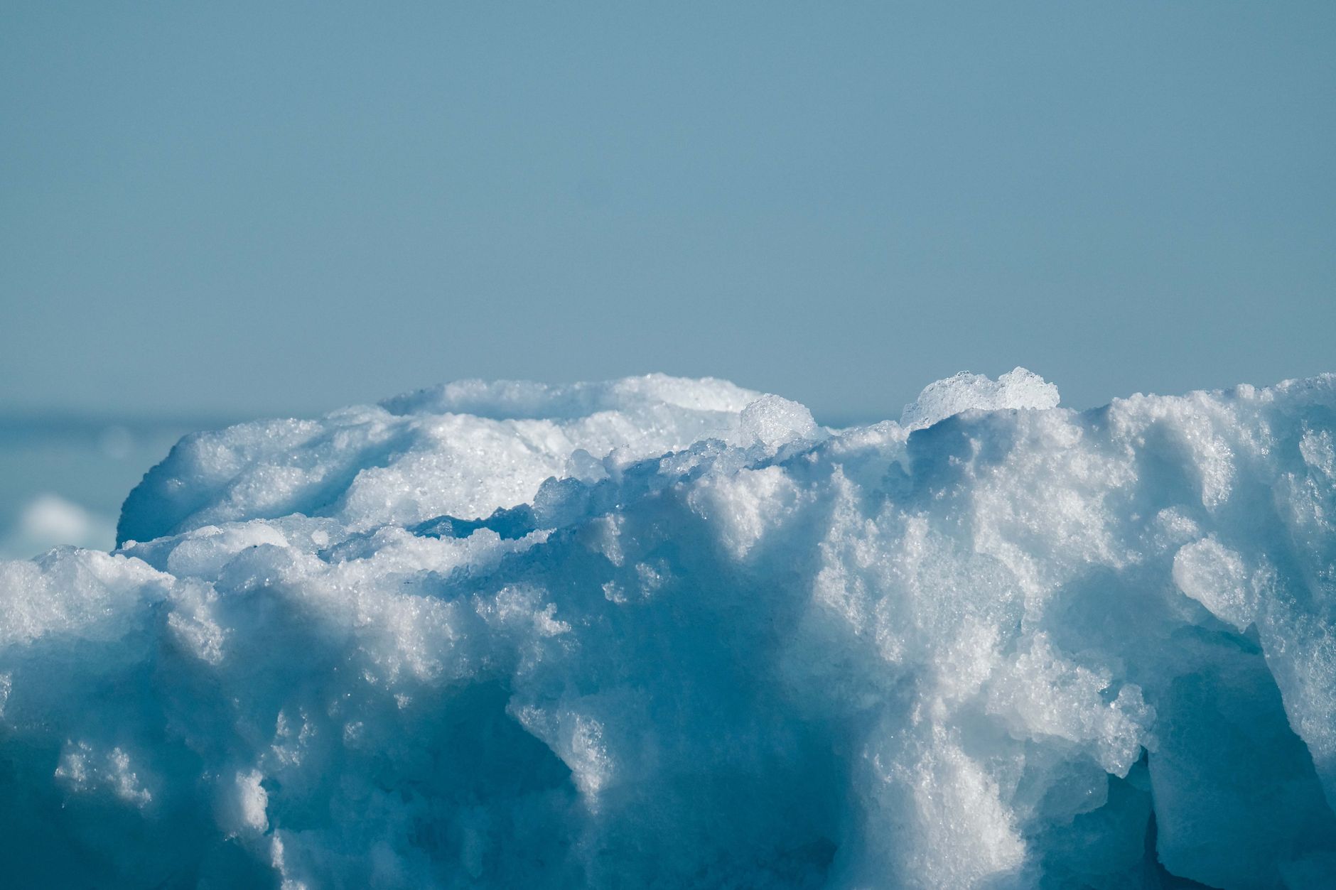A close-up shot of a large chunk of ice or snow against a pale blue background.
