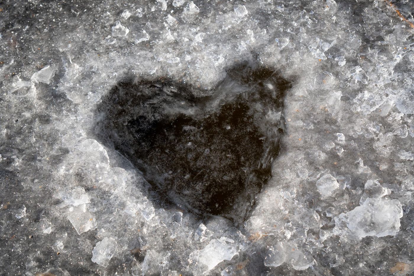 A heart-shaped hole in a sheet of ice, surrounded by slush and ice chunks.