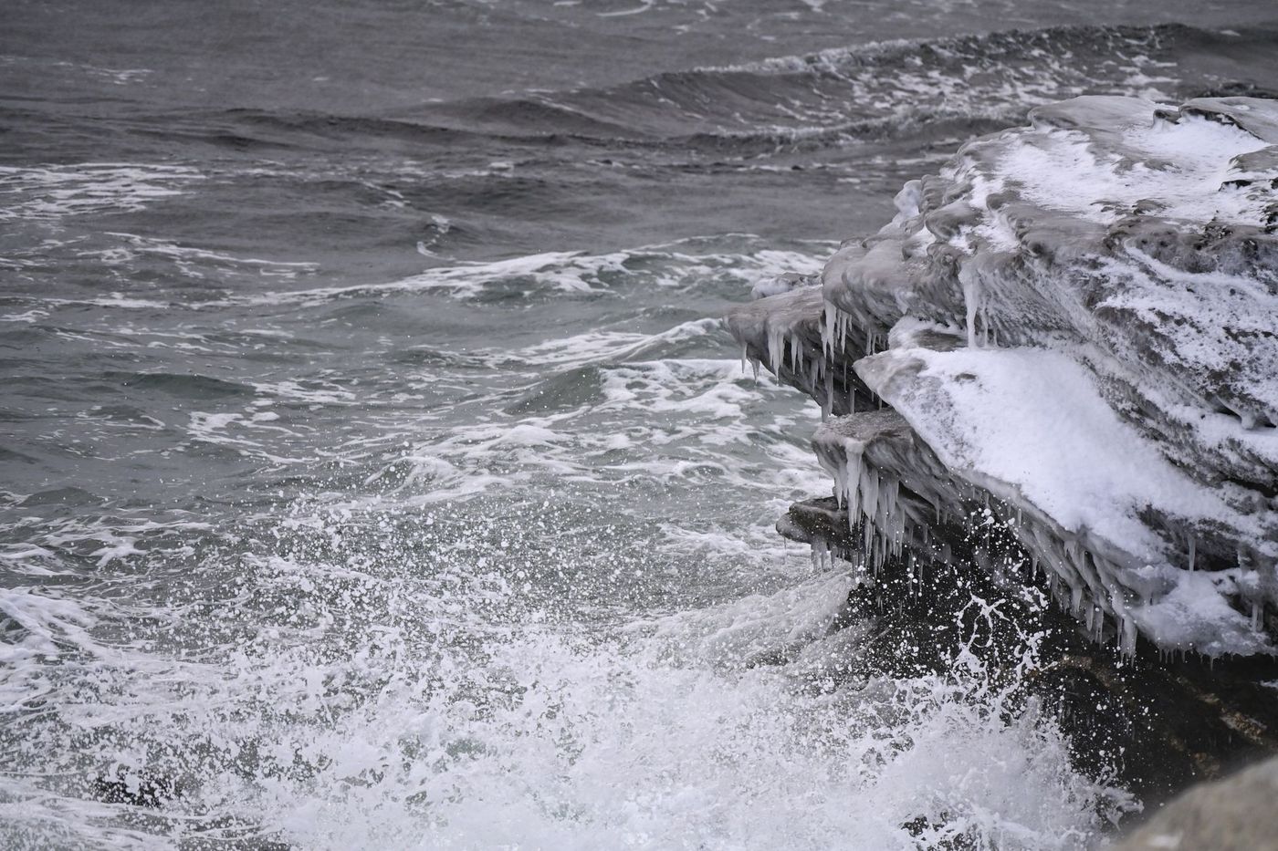 Dark sea waves crashing against icy rocks under a cold, overcast sky.