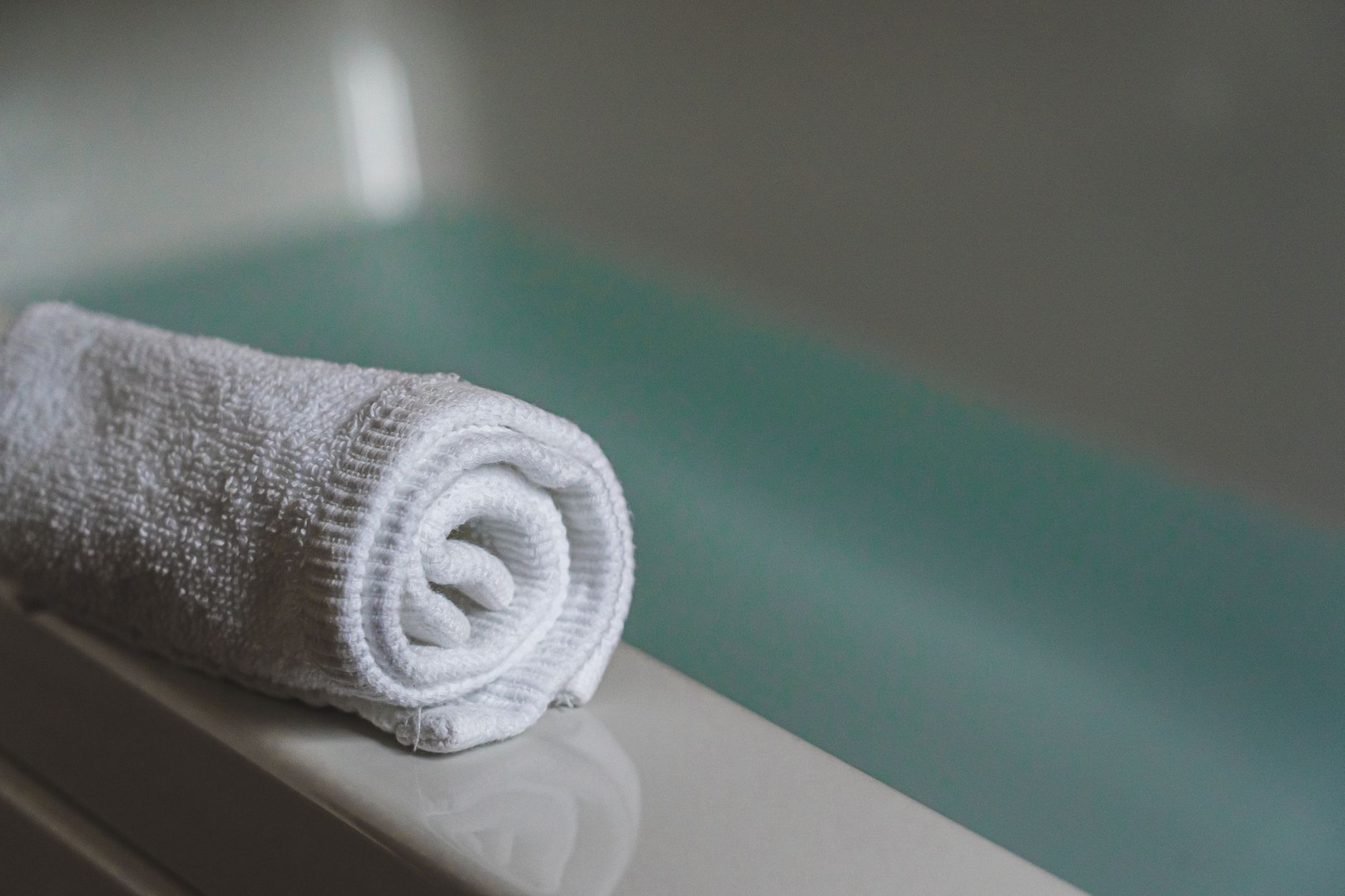 A close-up of a rolled white towel resting on the edge of a bathtub.