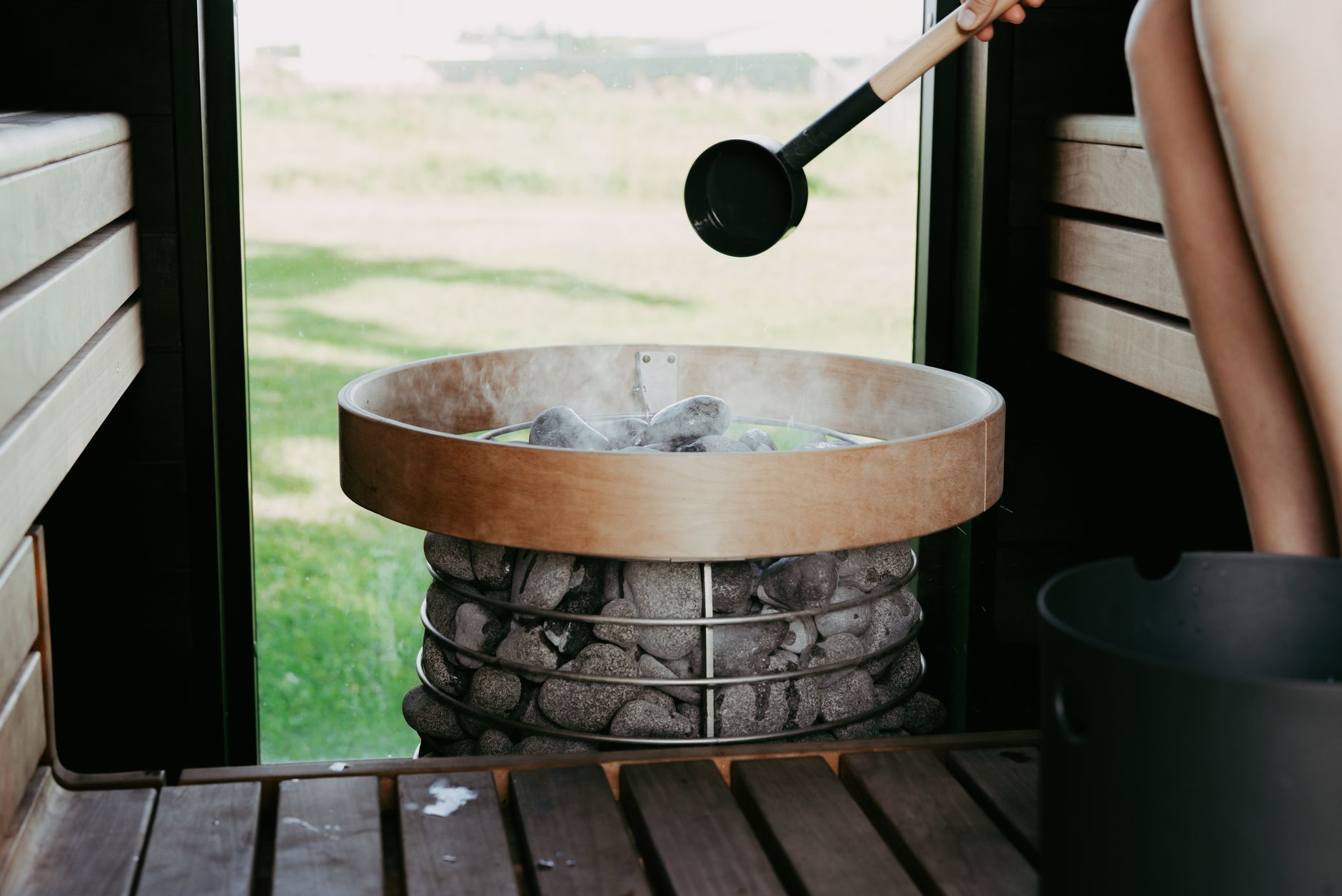 Man ladling water onto hot stones inside a cedar sauna room