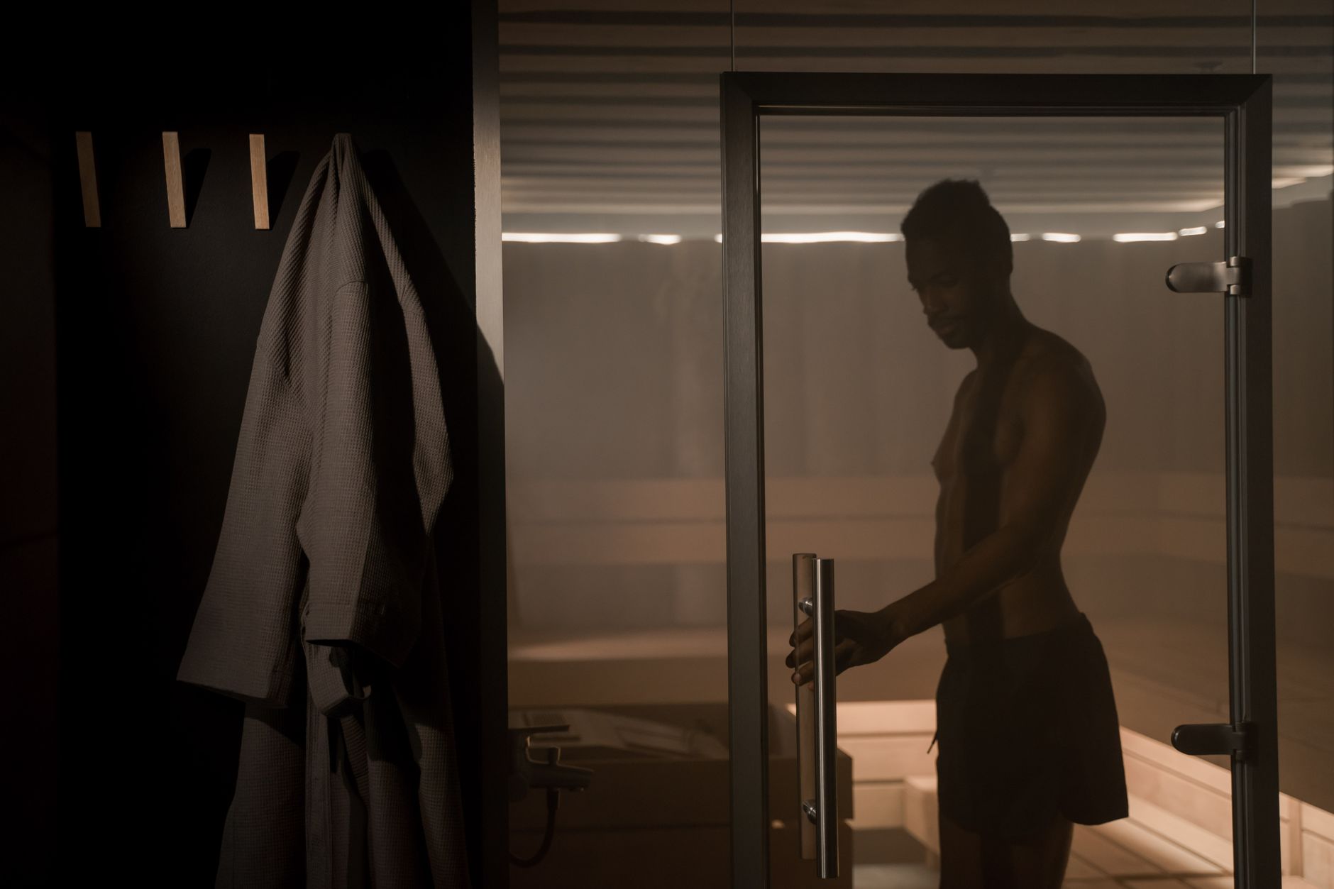 Man in swim shorts walking from a wooden sauna toward a cold plunge tub