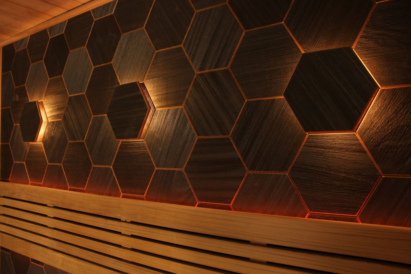 The interior of a modern sauna with wooden benches and a wall of dark, backlit hexagonal tiles.