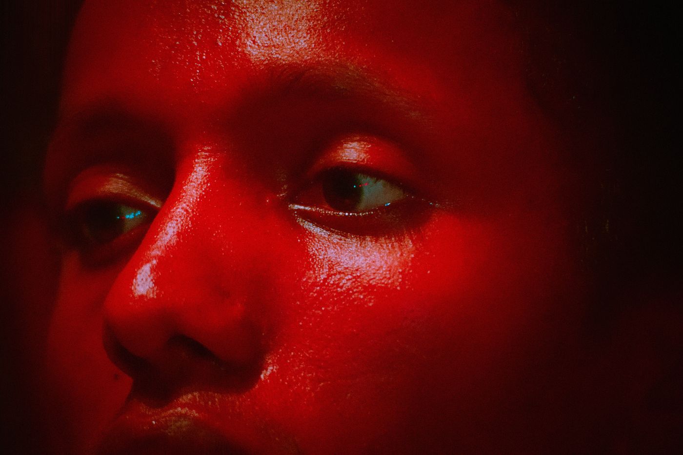 A close-up of a person's face illuminated by a strong red light, with their eyes open.
